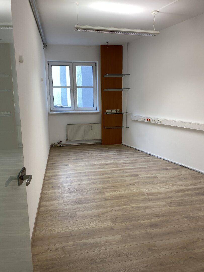 Kleiner Büroraum mit Fenster, Heizkörper, Laminatboden und praktischen Wandregalen an einer Holzsäule.