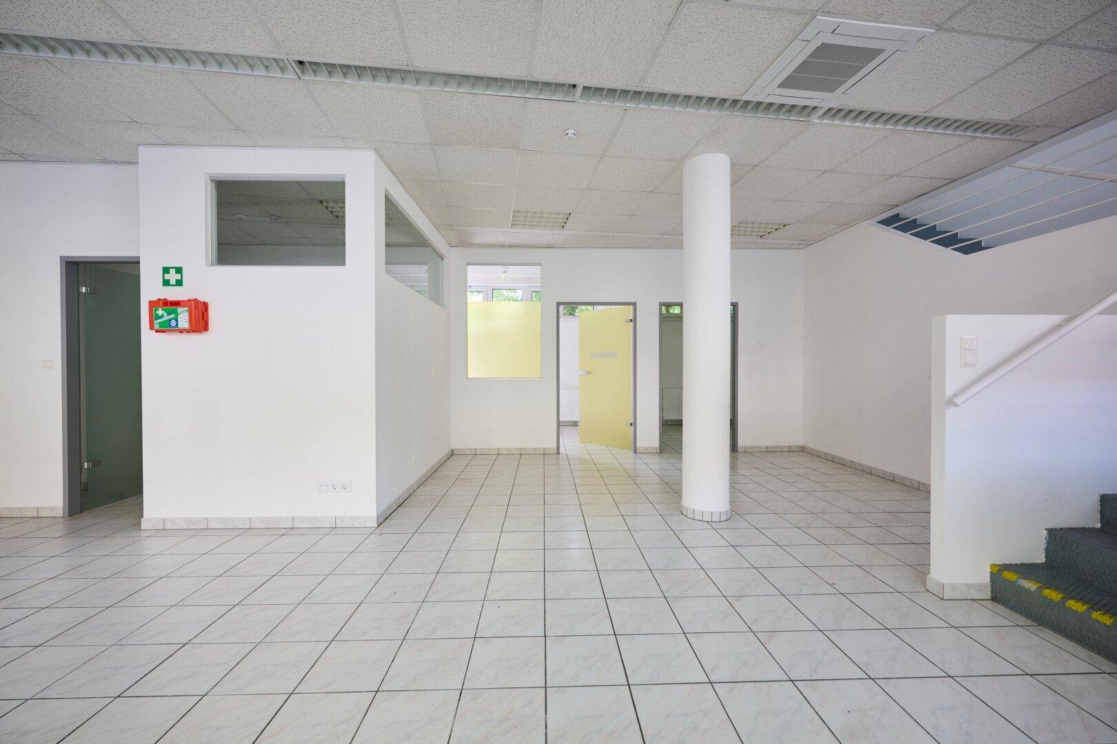 Offener Gewerberaum mit weißen Wänden, Fliesenboden und mehreren Türen zu angrenzenden Räumen.