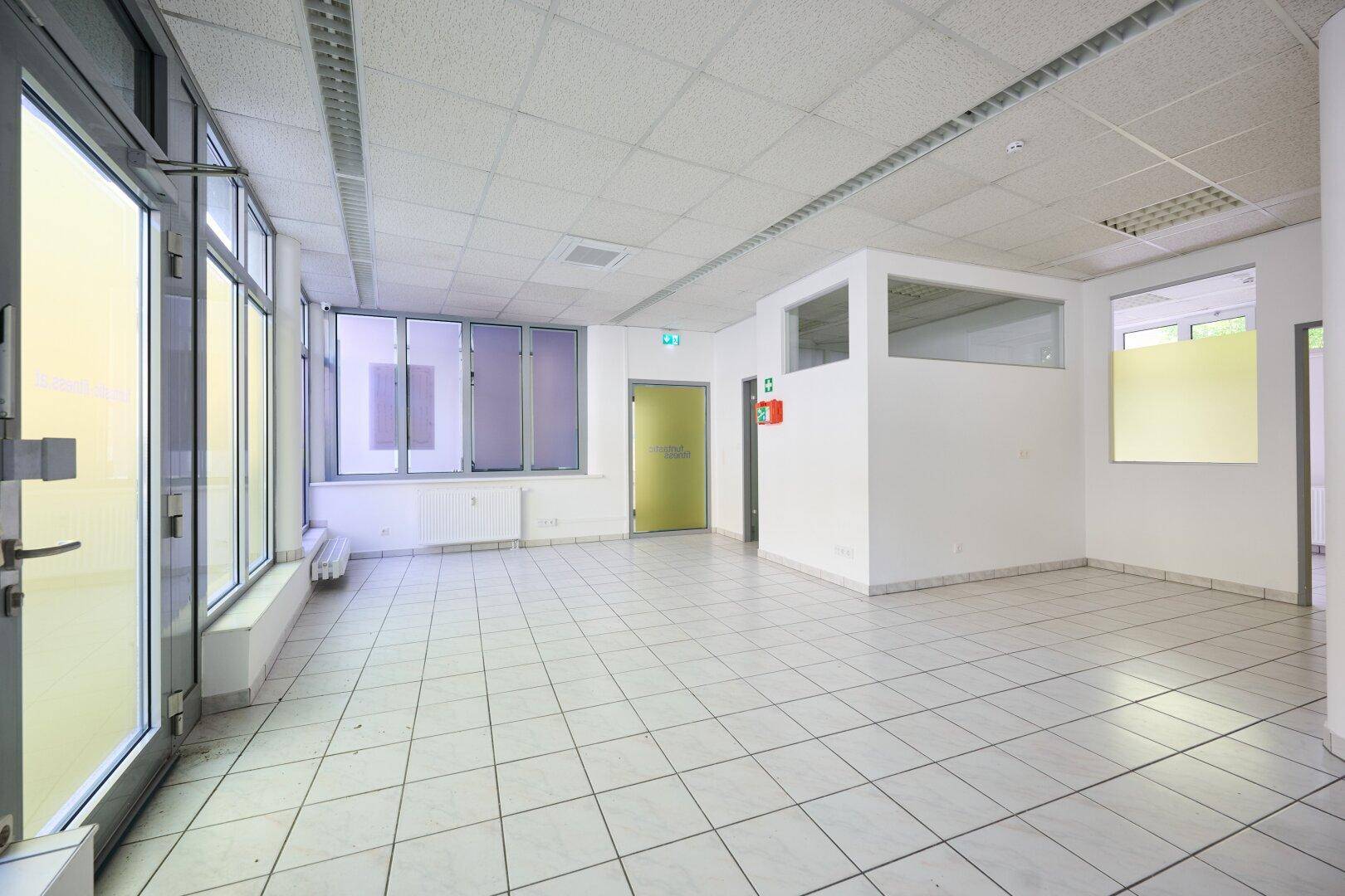 Geräumiger Gewerberaum mit Eingangstür, großen Fenstern und viel Tageslicht.