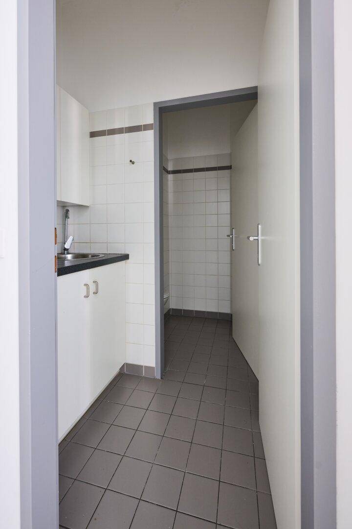 Kleine Küchenzeile mit Spüle, Unterschränken und grauem Fliesenboden.