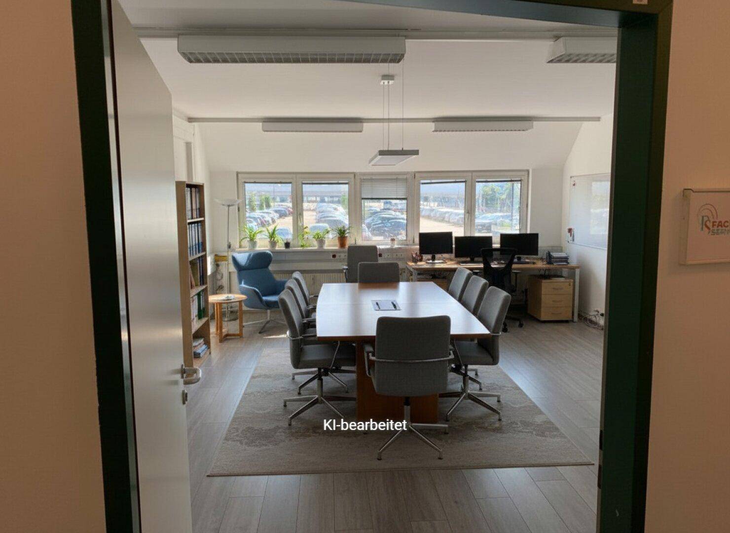 Großes, helles Büro mit Konferenztisch, Arbeitsplätzen und Blick auf den Parkplatz durch die Fenster.