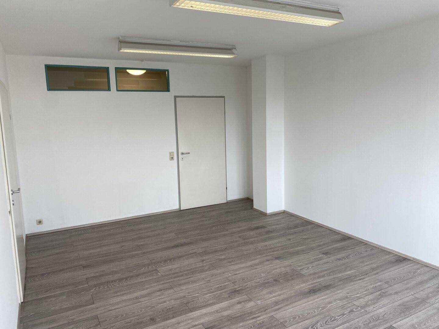 Leerer Raum mit zwei Türen und Oberlichtern, bietet Zugang zu weiteren Bereichen.