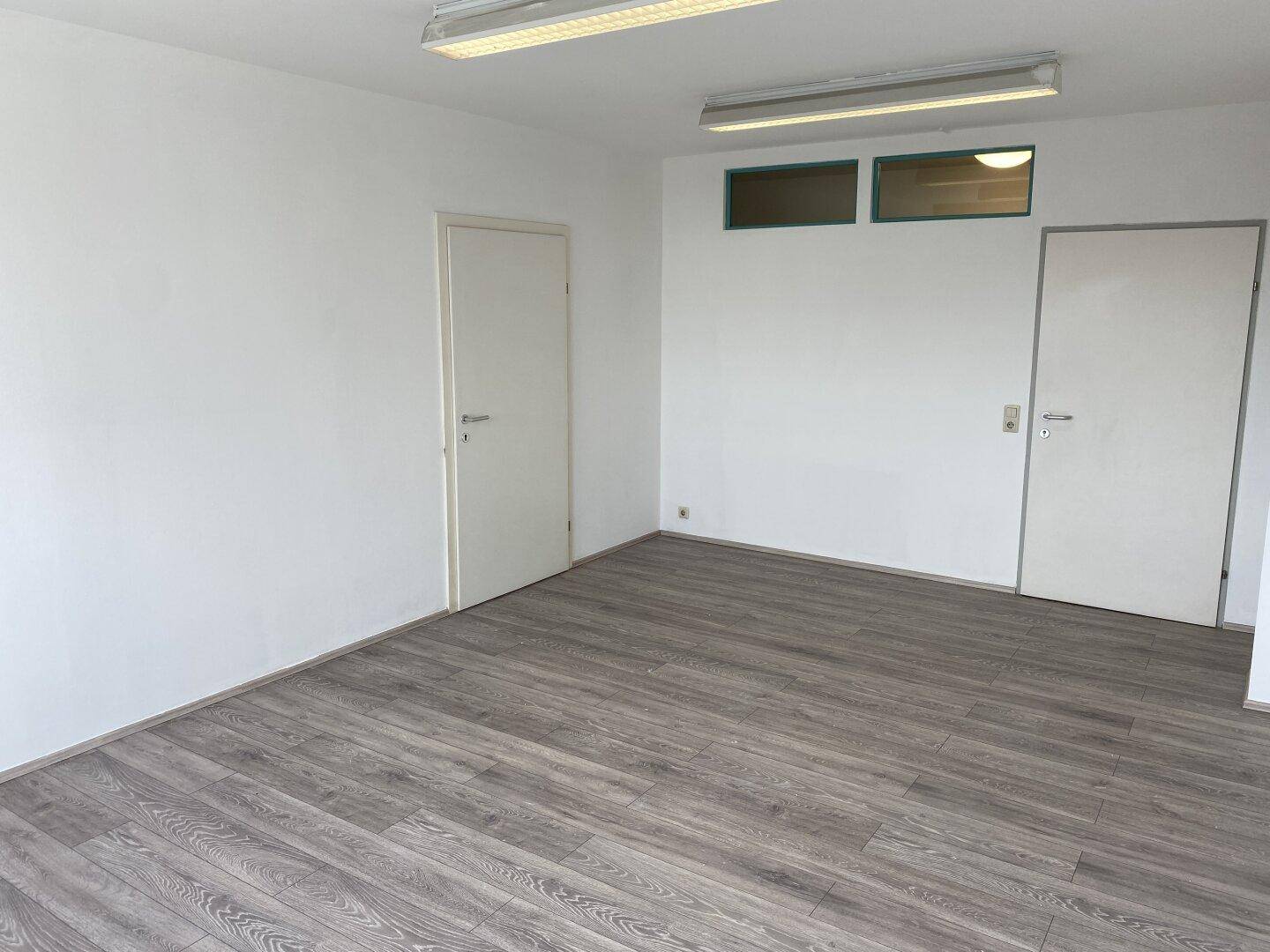 Geräumiger, leerer Raum mit zwei Türen und Deckenbeleuchtung, ideal für verschiedene Nutzungen.