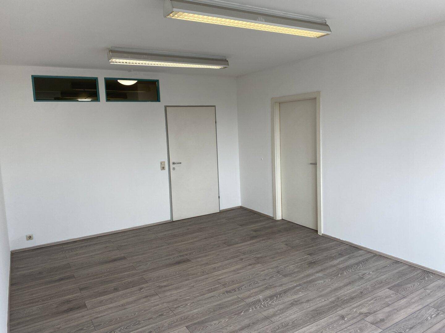 Leerer Raum mit Laminatboden, weißen Wänden und zwei Türen.