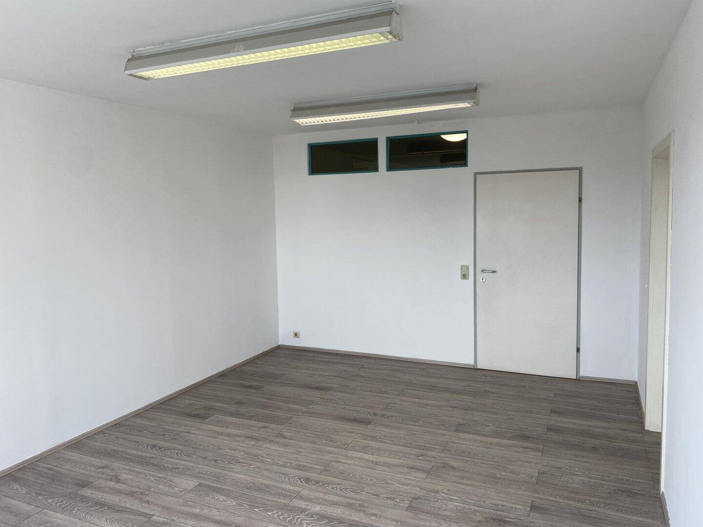 Leerer Raum mit Laminatboden, weißen Wänden und zwei Türen.