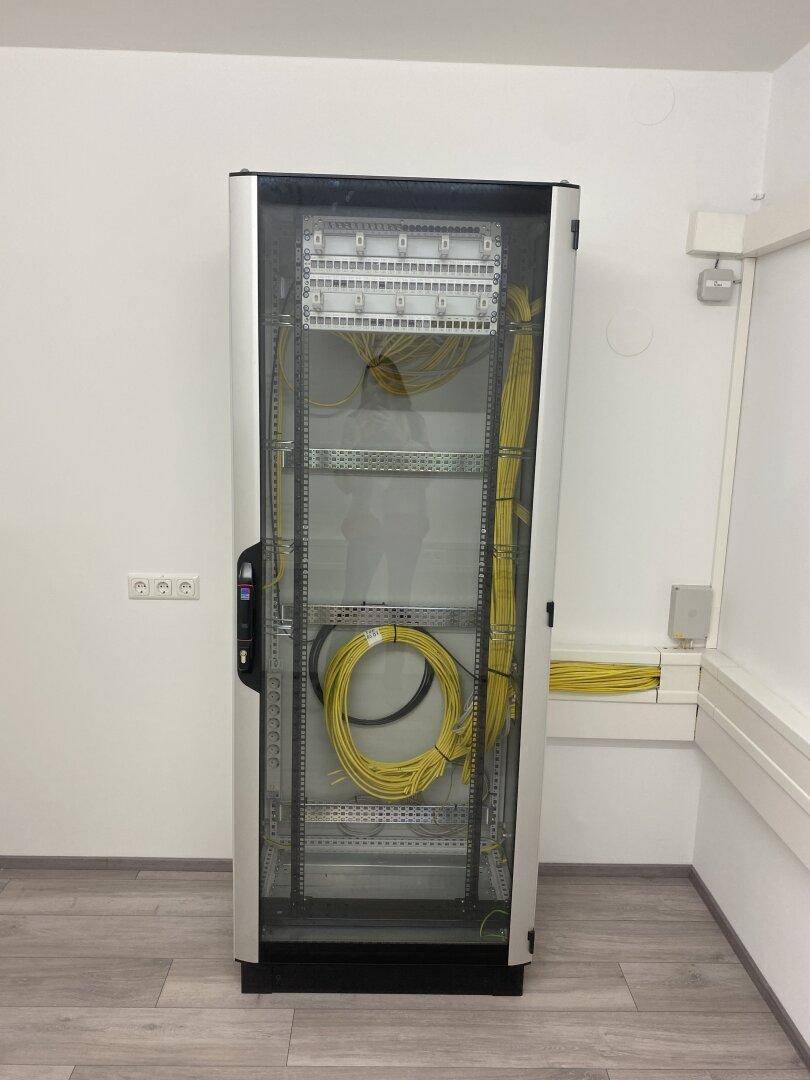 Technikraum mit Serverschrank und ordentlich verlegten Kabeln, bereit für IT-Infrastruktur.