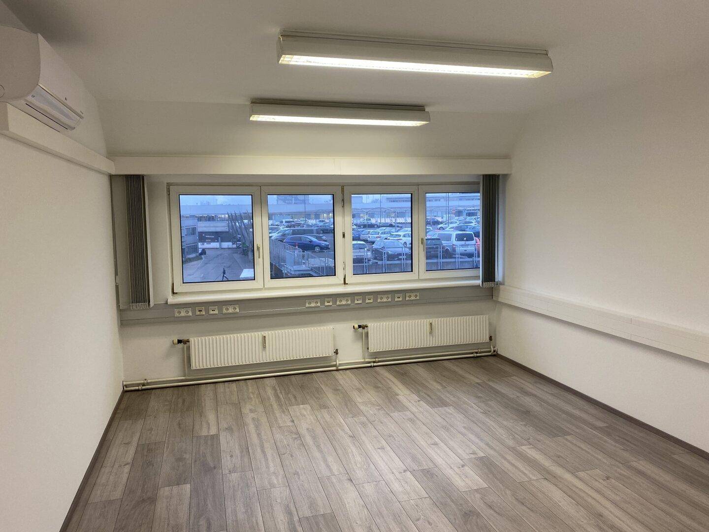 Geräumiges Büro mit Laminatboden, großen Fenstern und integrierter Klimaanlage für angenehmes Raumklima.