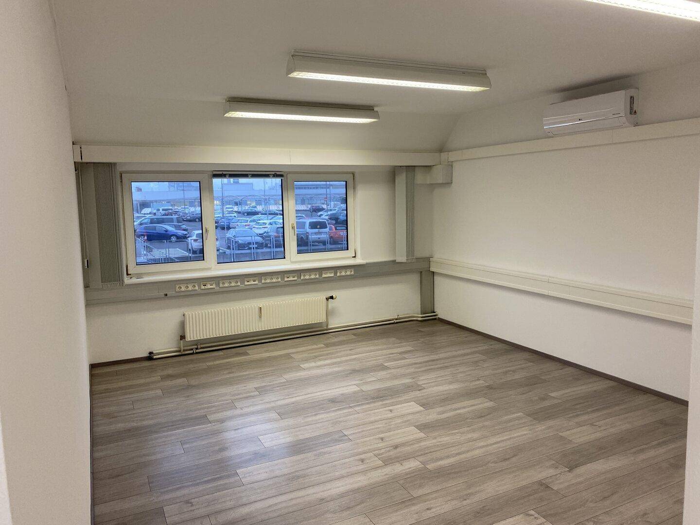 Modernes Büro mit hellem Laminatboden, großen Fenstern und Klimaanlage, bereit zur sofortigen Nutzung.