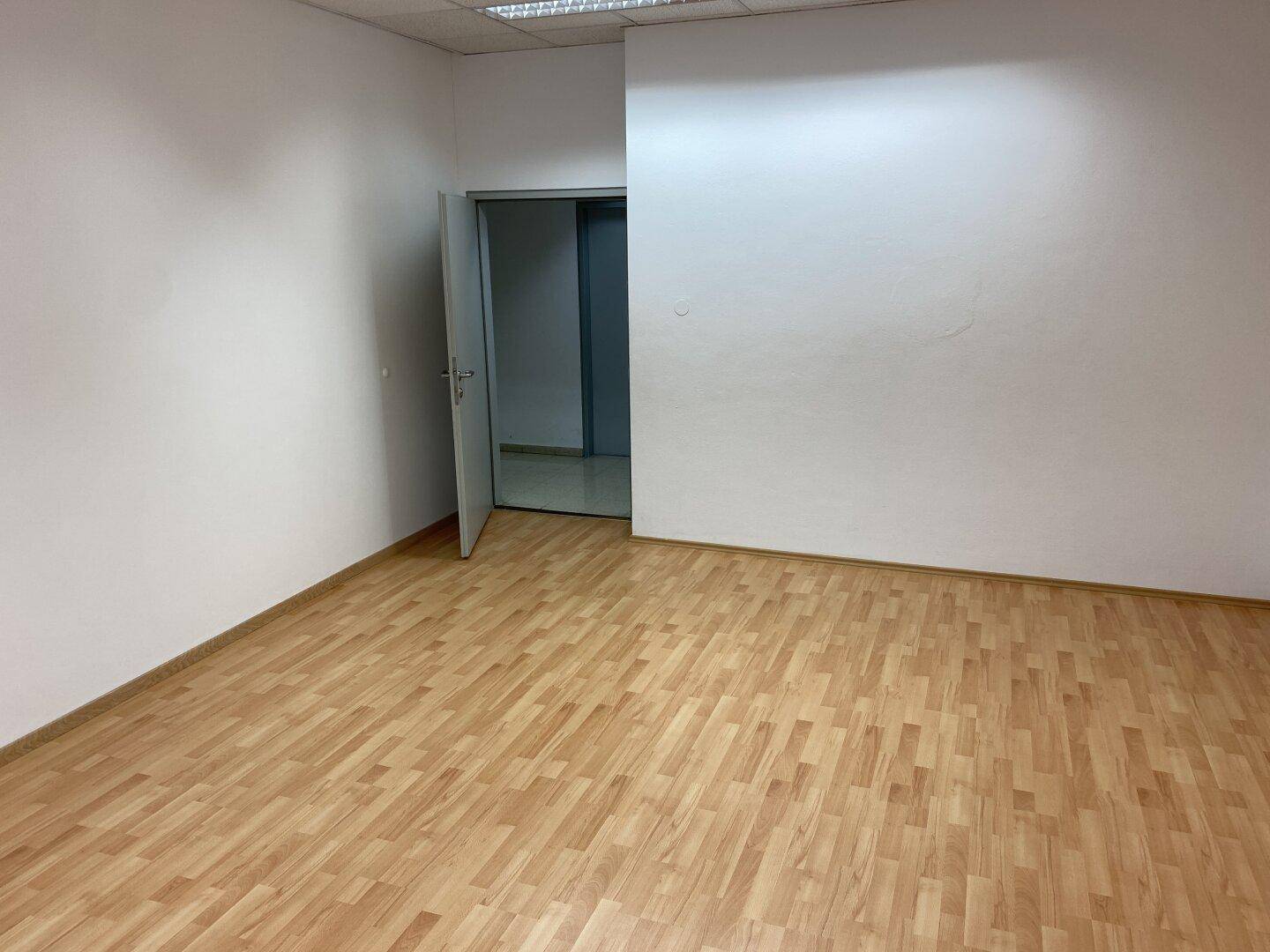 Leeres Büro mit Laminatboden und offener Tür zu einem weiteren Raum.