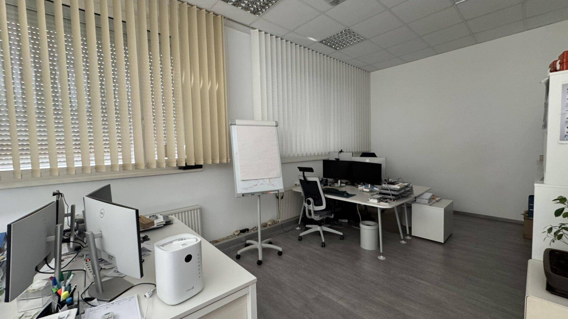 Modernes Büro mit mehreren Arbeitsplätzen, vertikalen Jalousien und grauem Laminatboden.