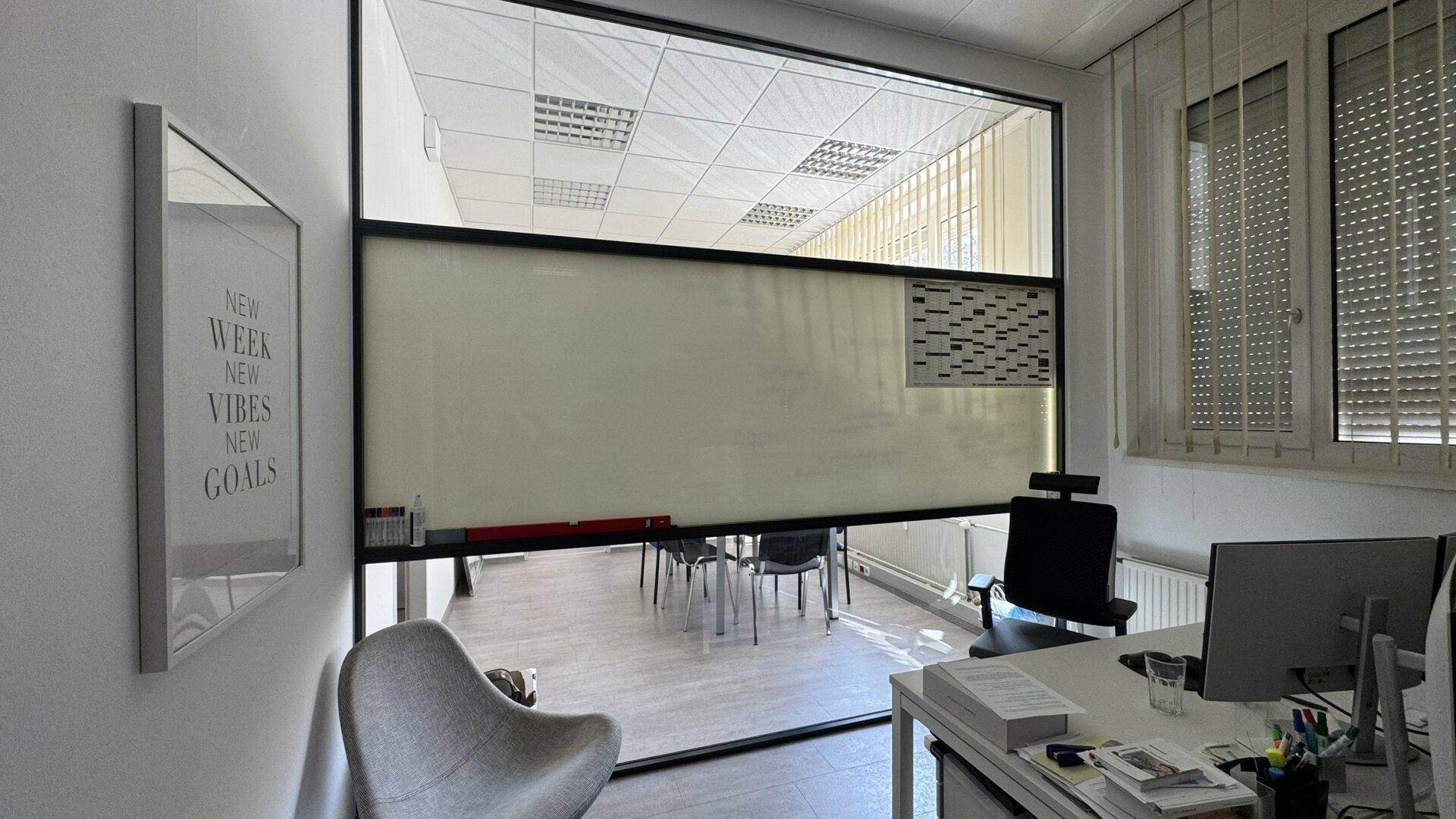 Büro mit Glaswand zu einem weiteren Raum, modernem Dekor und vertikalen Jalousien am Fenster.