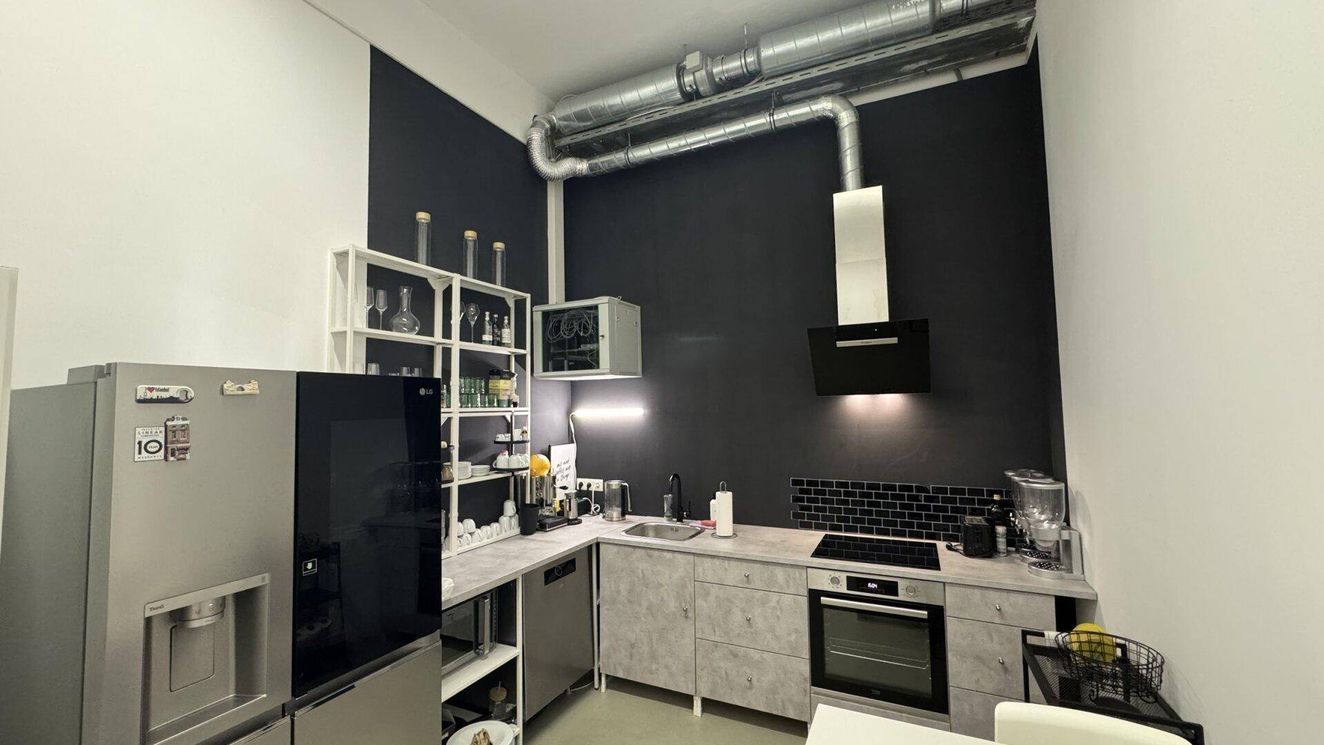 Moderne Küche mit schwarzen und weißen Wänden, Edelstahlgeräten und sichtbaren Lüftungsrohren.
