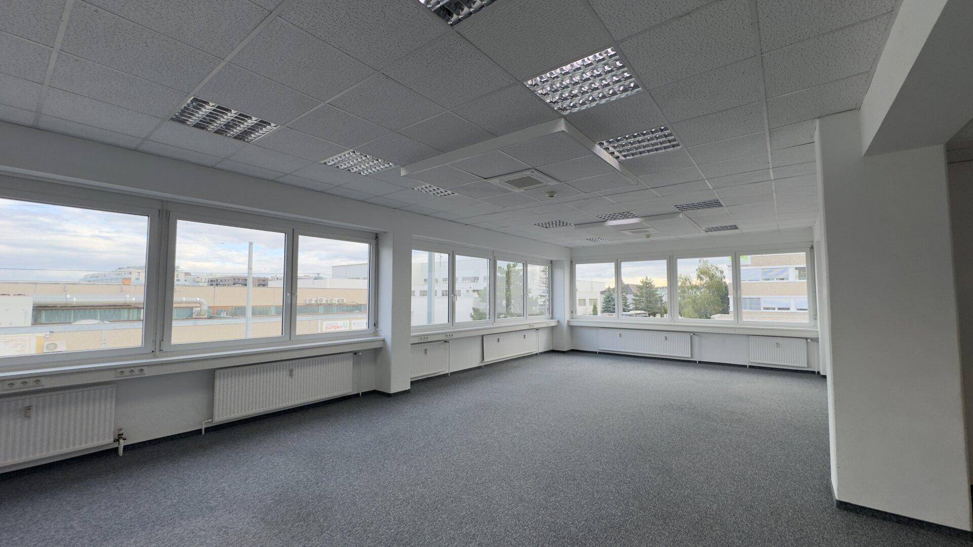 Geräumiges, leeres Büro mit großen Fenstern, Teppichboden und abgehängter Decke, bereit zur Einrichtung.