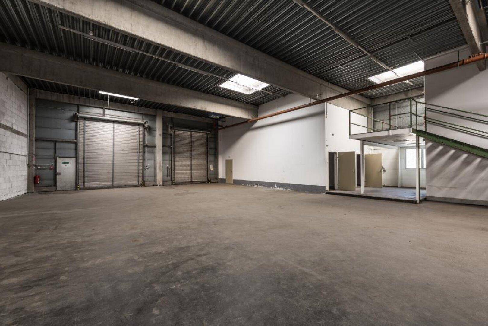 Große Lagerhalle mit Rolltoren, Betonboden und einer erhöhten Plattform mit Treppenzugang.