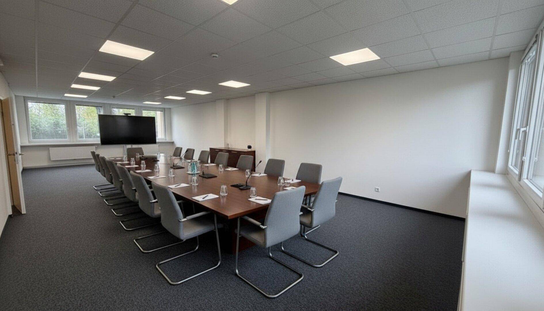 Großer Konferenzraum mit langem Holztisch, vielen Stühlen und Teppichboden.