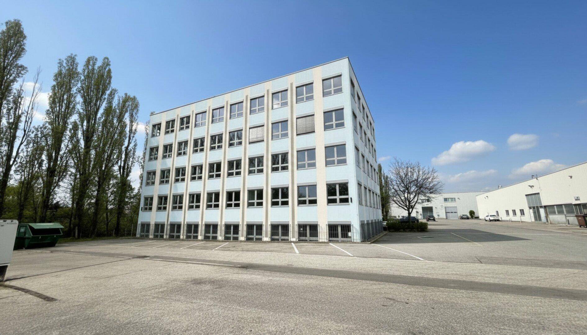 Freistehendes Bürogebäude mit vielen Fenstern und weitläufigem Parkplatzbereich.