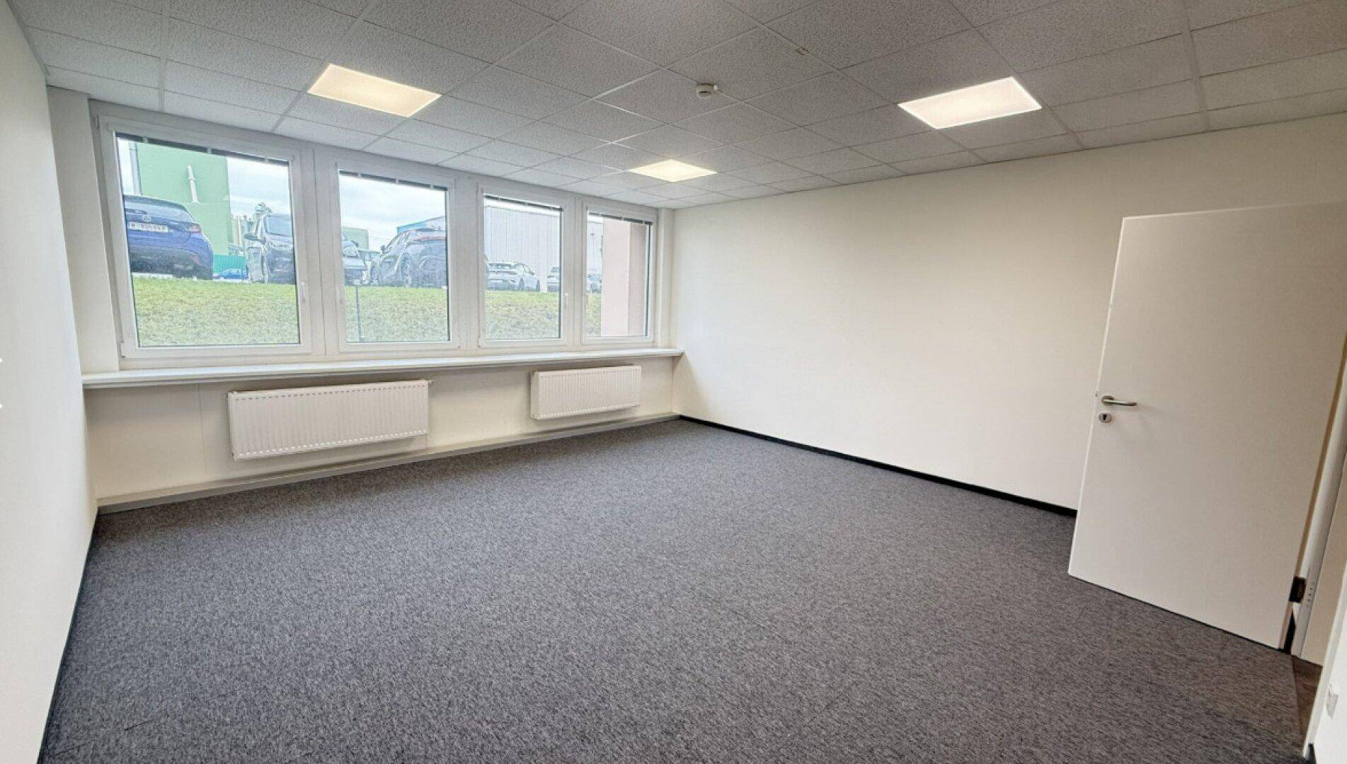 Helles und leeres Büro mit großen Fenstern und Heizkörpern unter der Fensterbank.