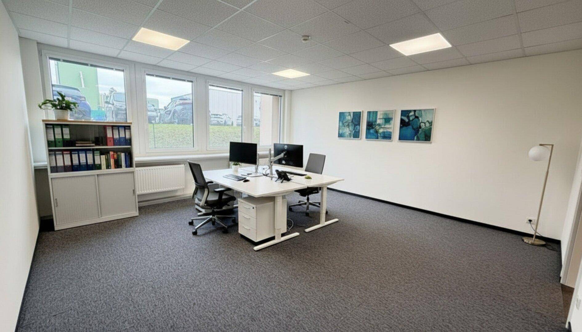 Helles Büro mit Teppichboden, modernen Möbeln und großen Fenstern.