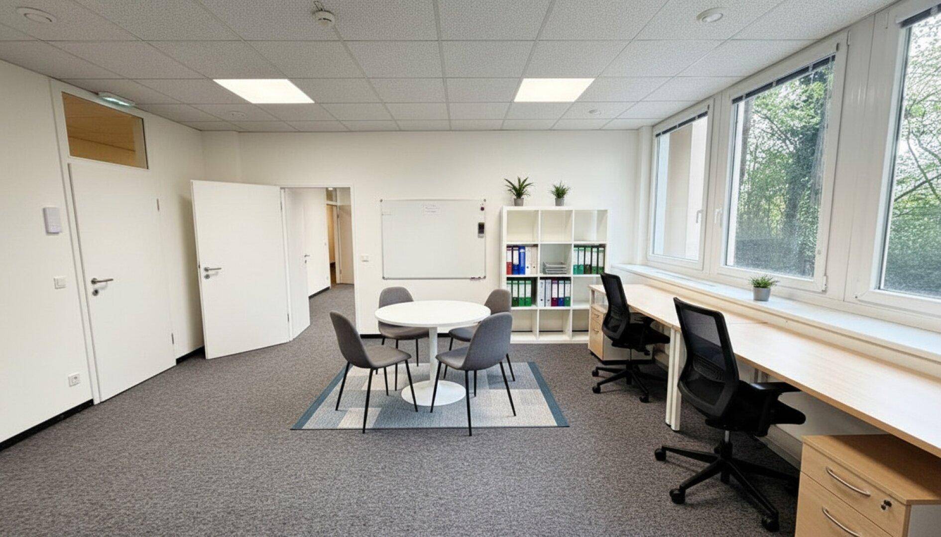 Geräumiges Büro mit Teppichboden, großen Fenstern und modernen Büromöbeln.