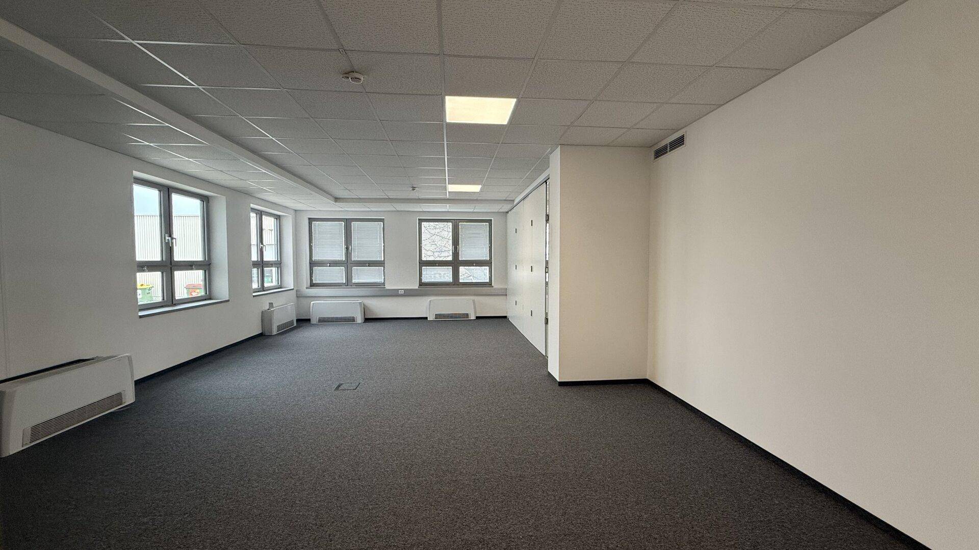 Großes, leeres Büro mit Teppichboden, vielen Fenstern und Jalousien, bereit zur individuellen Gestaltung.