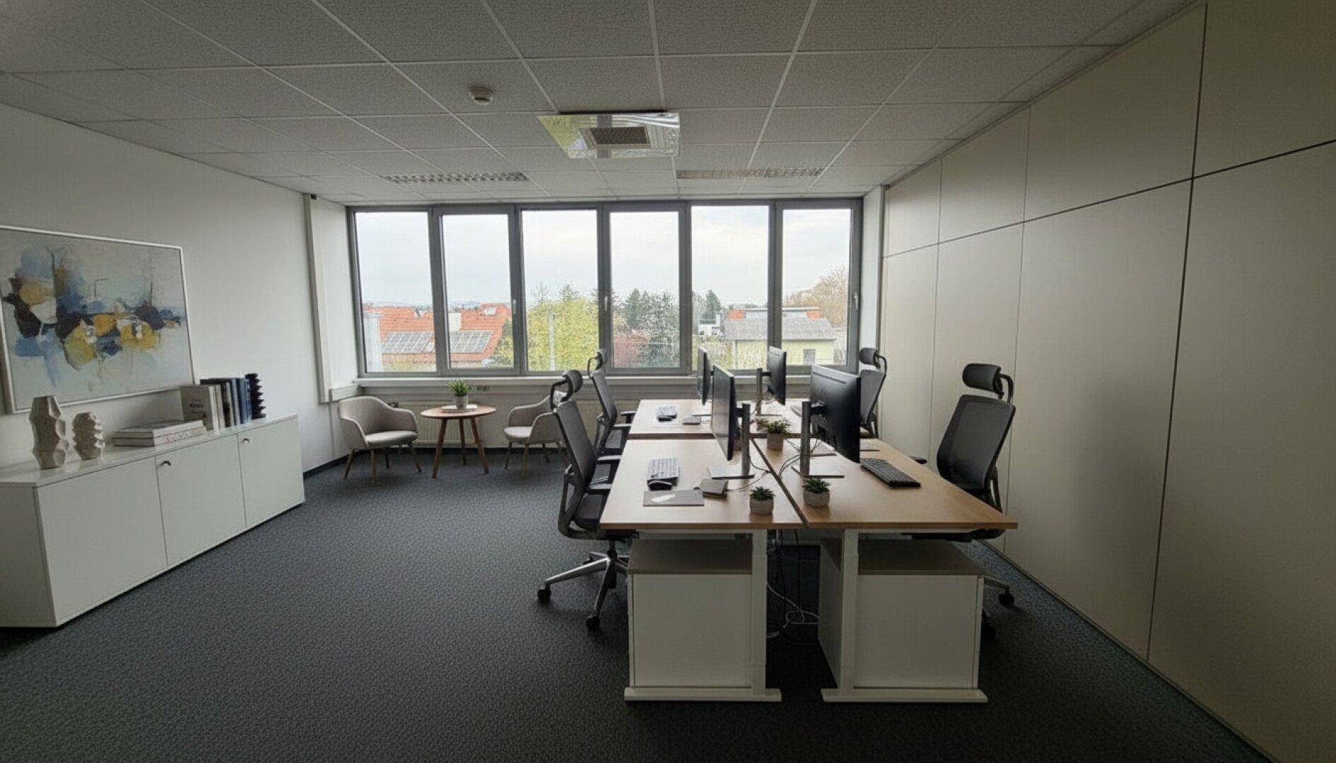 Helles und modernes Büro mit mehreren Arbeitsplätzen, großen Fenstern und Blick auf die Umgebung.