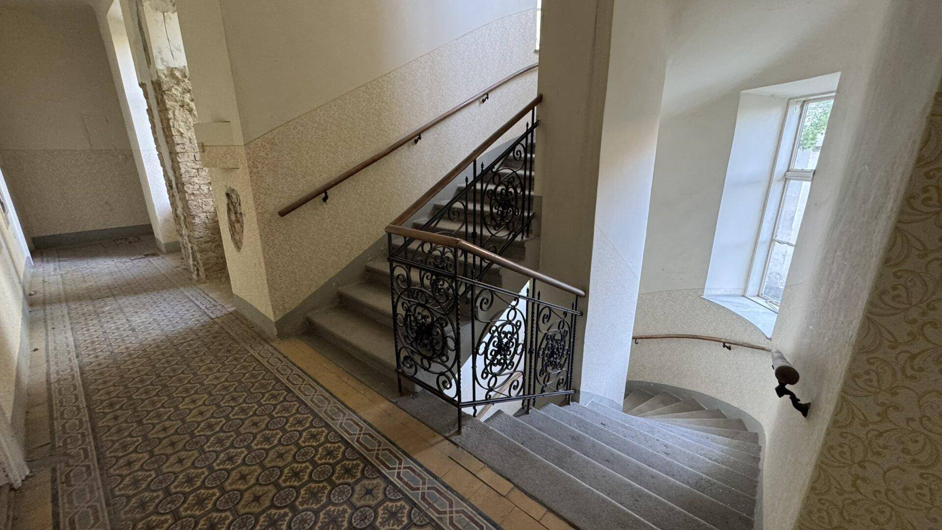 Historisches Treppenhaus mit schmiedeeisernem Geländer und gemustertem Bodenbelag in einem Altbau.