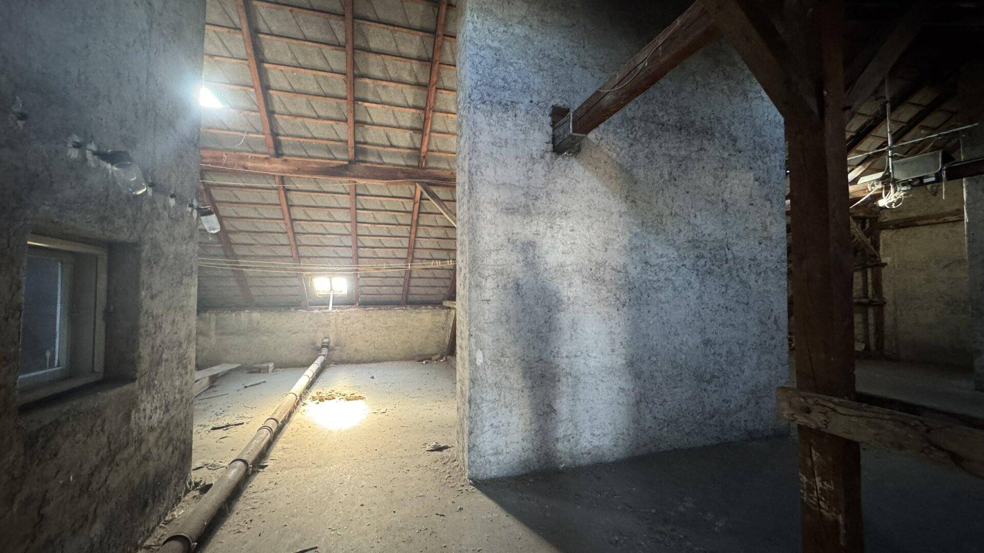 Unausgebauter Dachboden mit sichtbarer Holzkonstruktion und kleinen Fenstern, bietet Ausbaupotenzial.