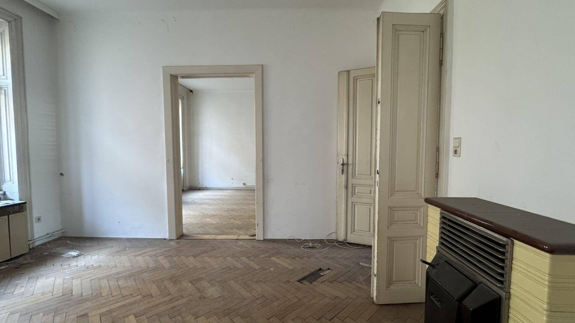 Geräumiges Zimmer mit Fischgrätparkett und einem alten Ofen, ideal für eine Neugestaltung.