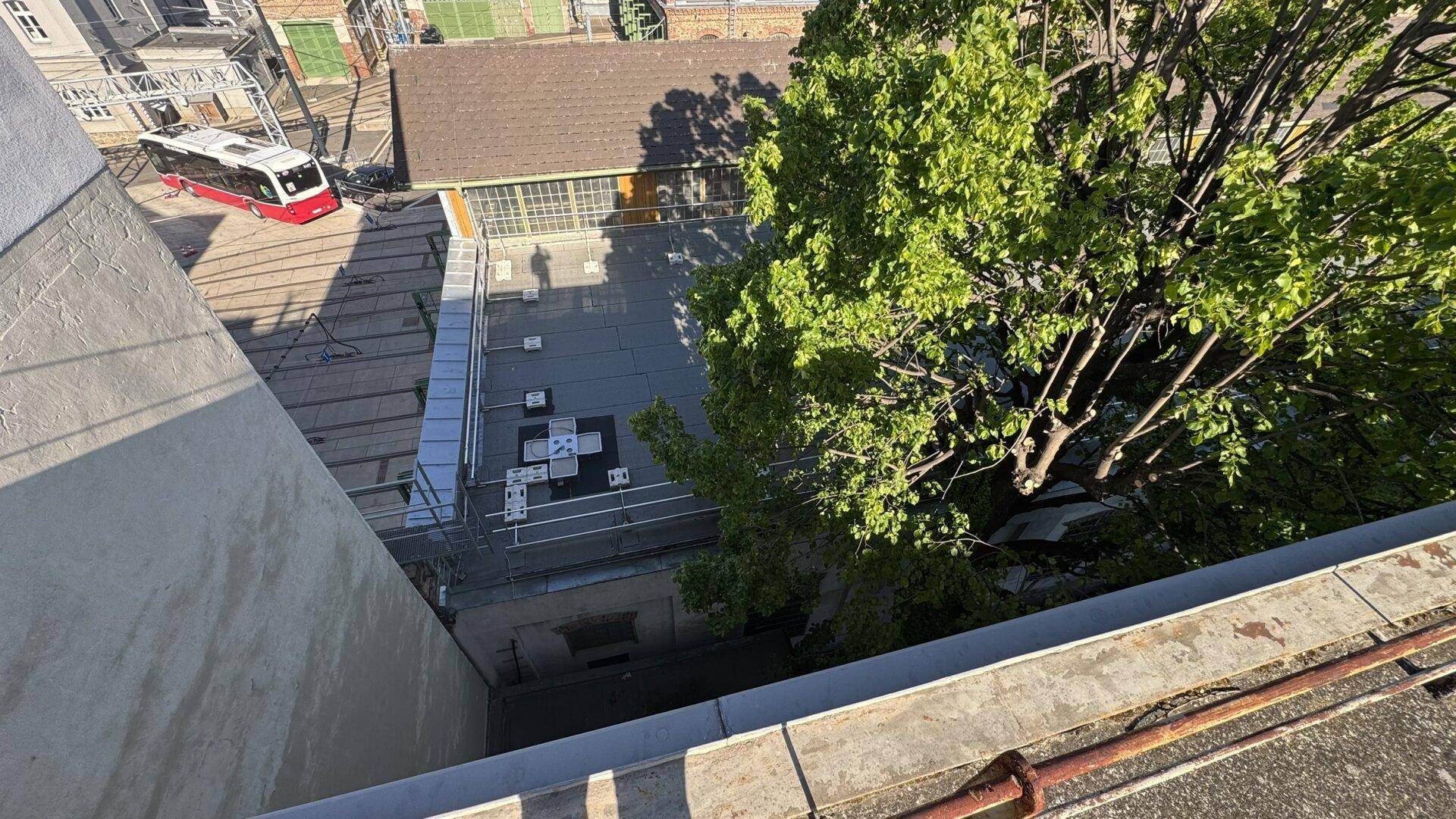 Aussicht von oben auf die Straße mit einer vorbeifahrenden Straßenbahn und grünen Bäumen.