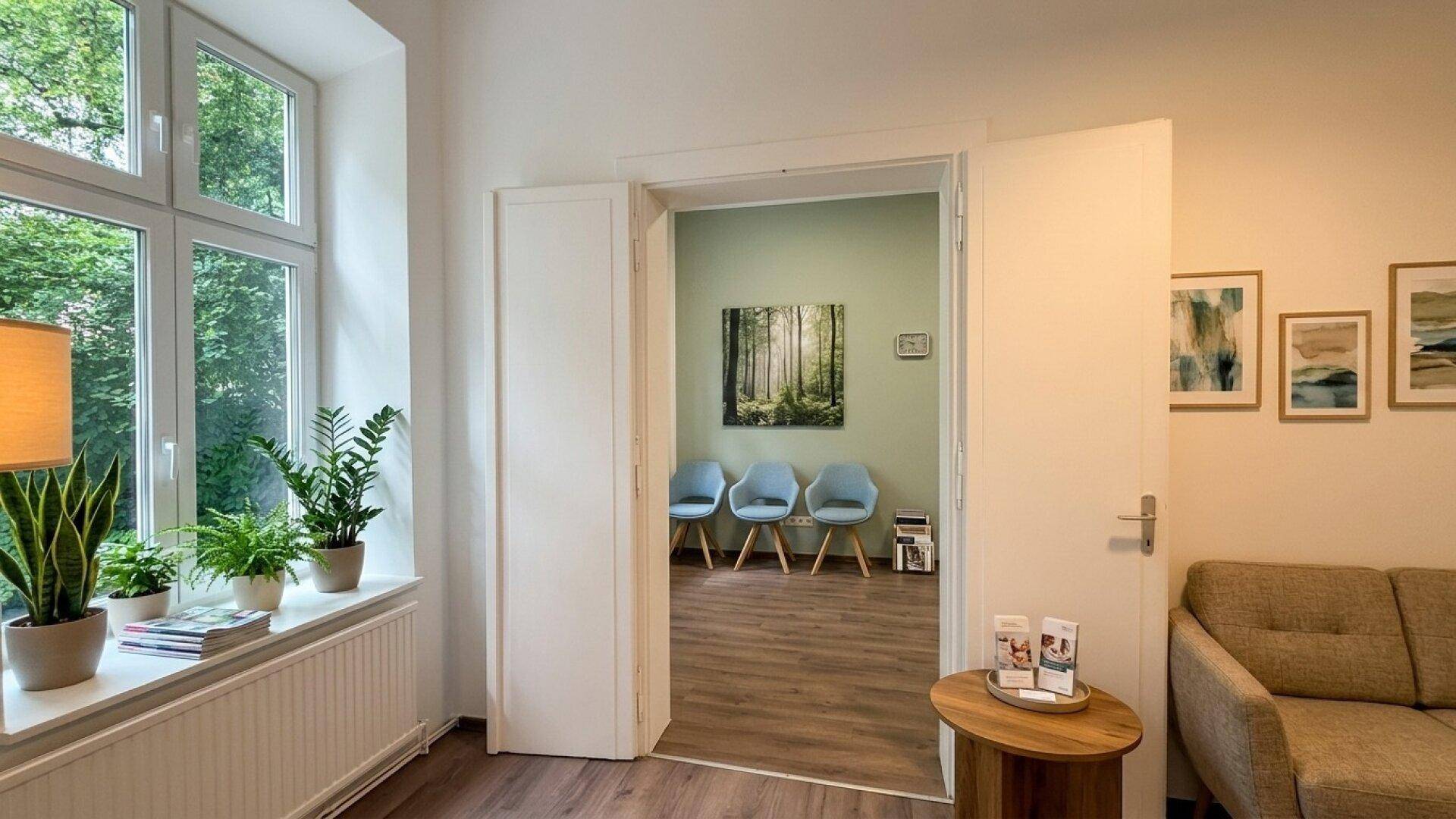 Gemütlicher Wartebereich mit Sofa, Pflanzen am Fenster und Blick in einen weiteren Raum.