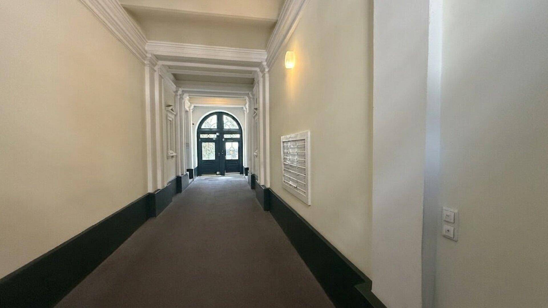 Eleganter Flur mit Stuckverzierungen, dunklem Teppichboden und einer großen, gewölbten Eingangstür.