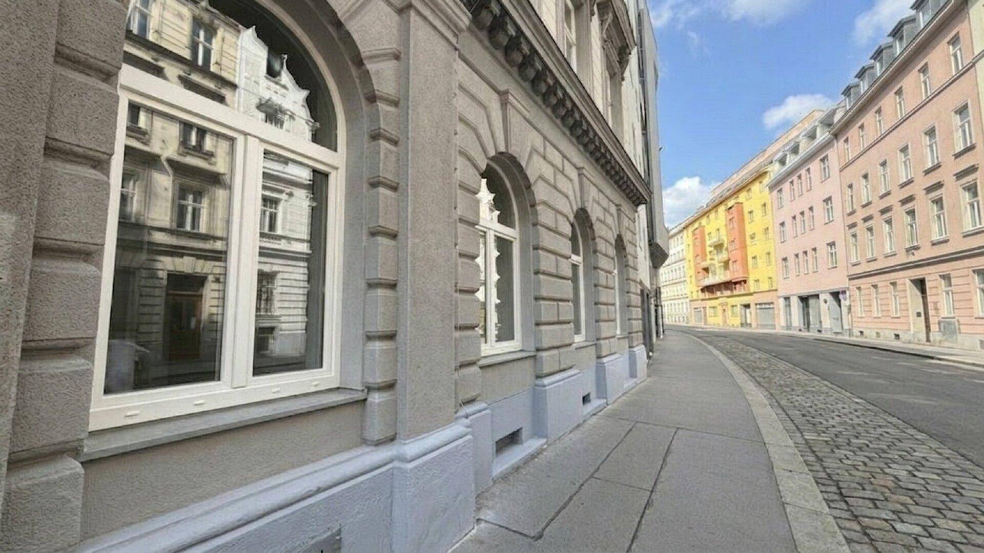 Historische Gebäudefassade mit Bogenfenstern und klassischer Architektur an einer städtischen Straße.