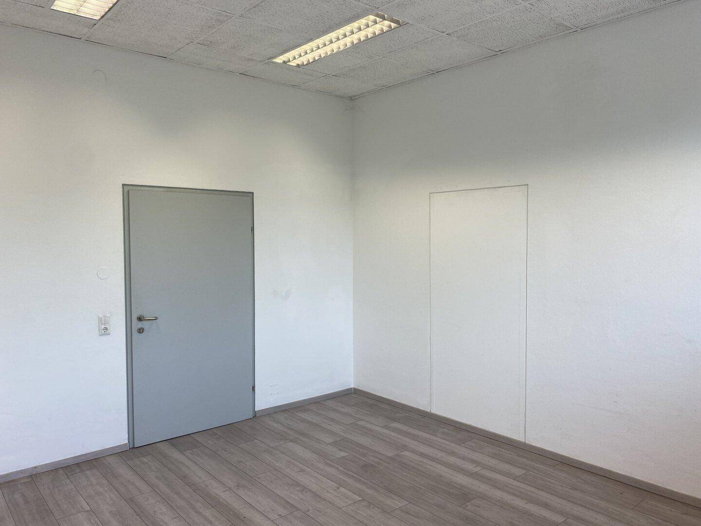 Geräumiges, leeres Büro mit Laminatboden und zwei Türen, bereit für die Büroeinrichtung.
