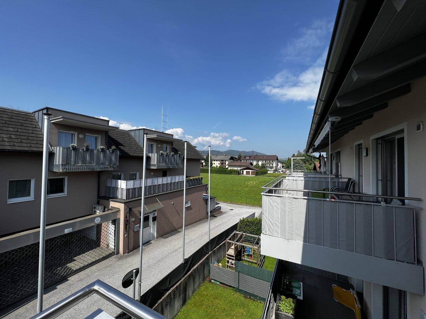 Weitblick vom Balkon über grüne Felder und die umliegende Wohnbebauung an einem sonnigen Tag.
