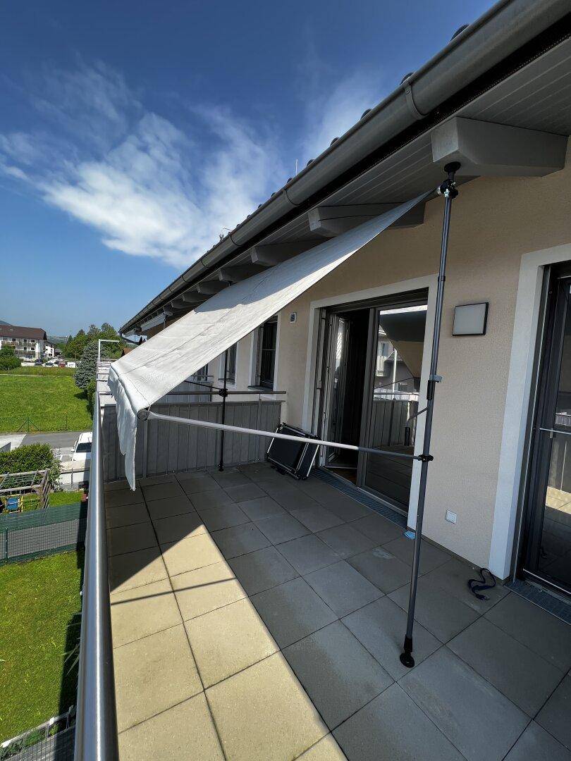 Geräumiger Balkon mit Fliesenboden, Markise und Blick ins Grüne.