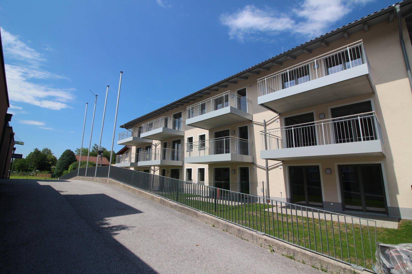 Modernes Mehrfamilienhaus mit mehreren Balkonen und barrierefreiem Zugang über eine Rampe.