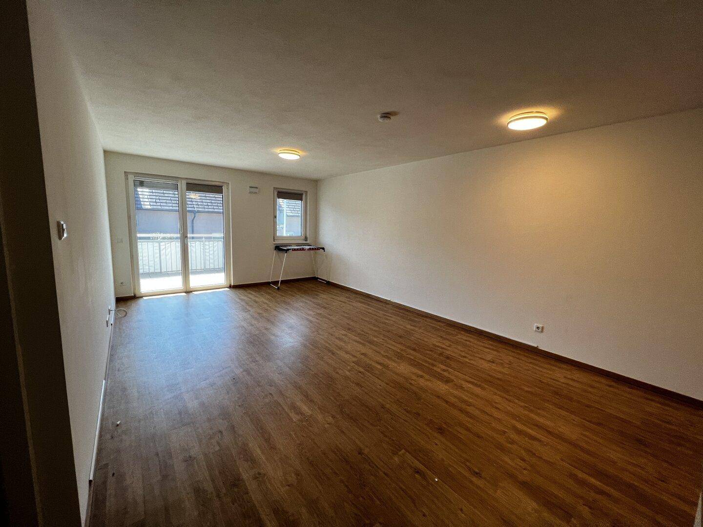 Geräumiger, heller Wohnraum mit Laminatboden und Zugang zu einem Balkon.