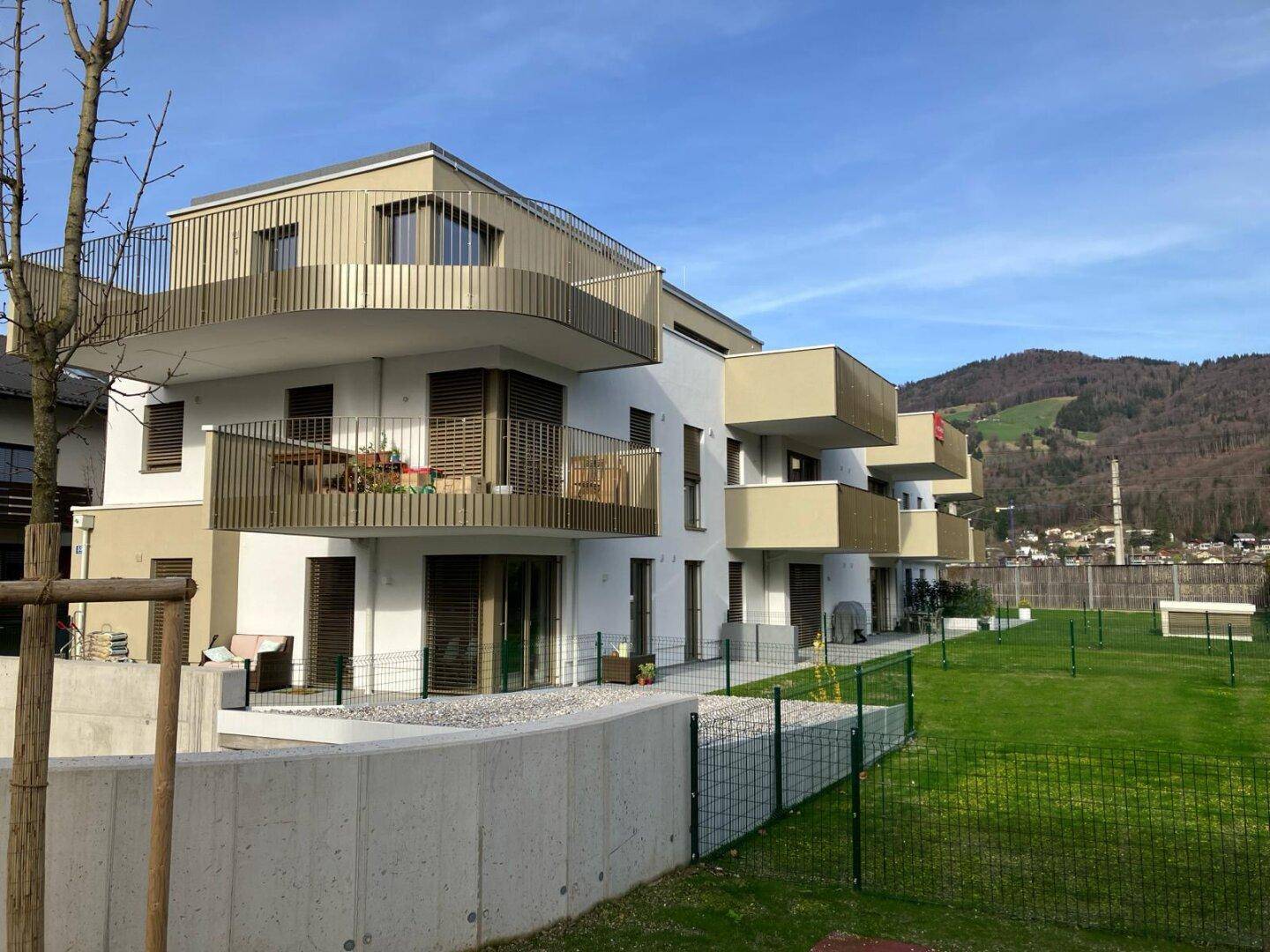 Moderne Wohnanlage mit mehreren Balkonen und gepflegten Grünflächen vor einer Hügellandschaft.
