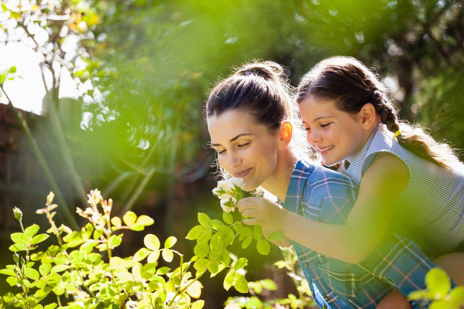 Mutter und Kind genießen den Duft einer weißen Blüte in einem sonnigen Garten.