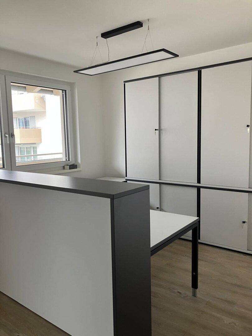 Heller Büroraum mit Fenster, moderner Theke und weißen Schränken.