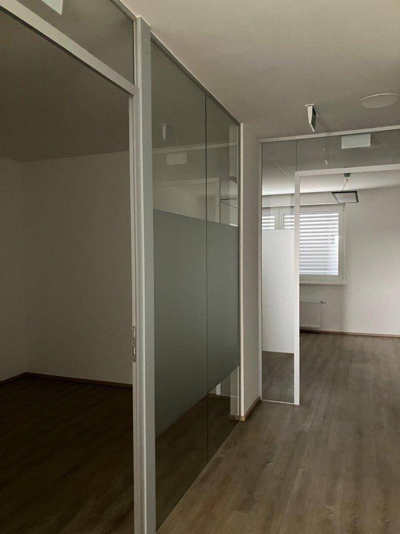 Moderner Bürogang mit Glaswänden und Jalousien an den Fenstern.