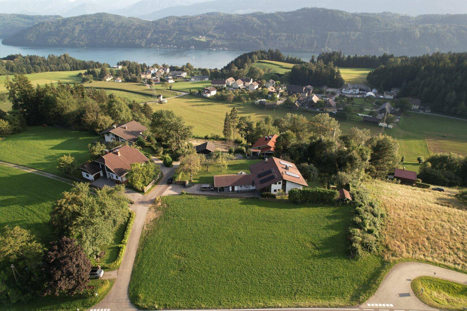 Näherer Luftbildblick auf eine idyllische Seenlandschaft mit bewaldeten Hügeln und Wohngebäuden.