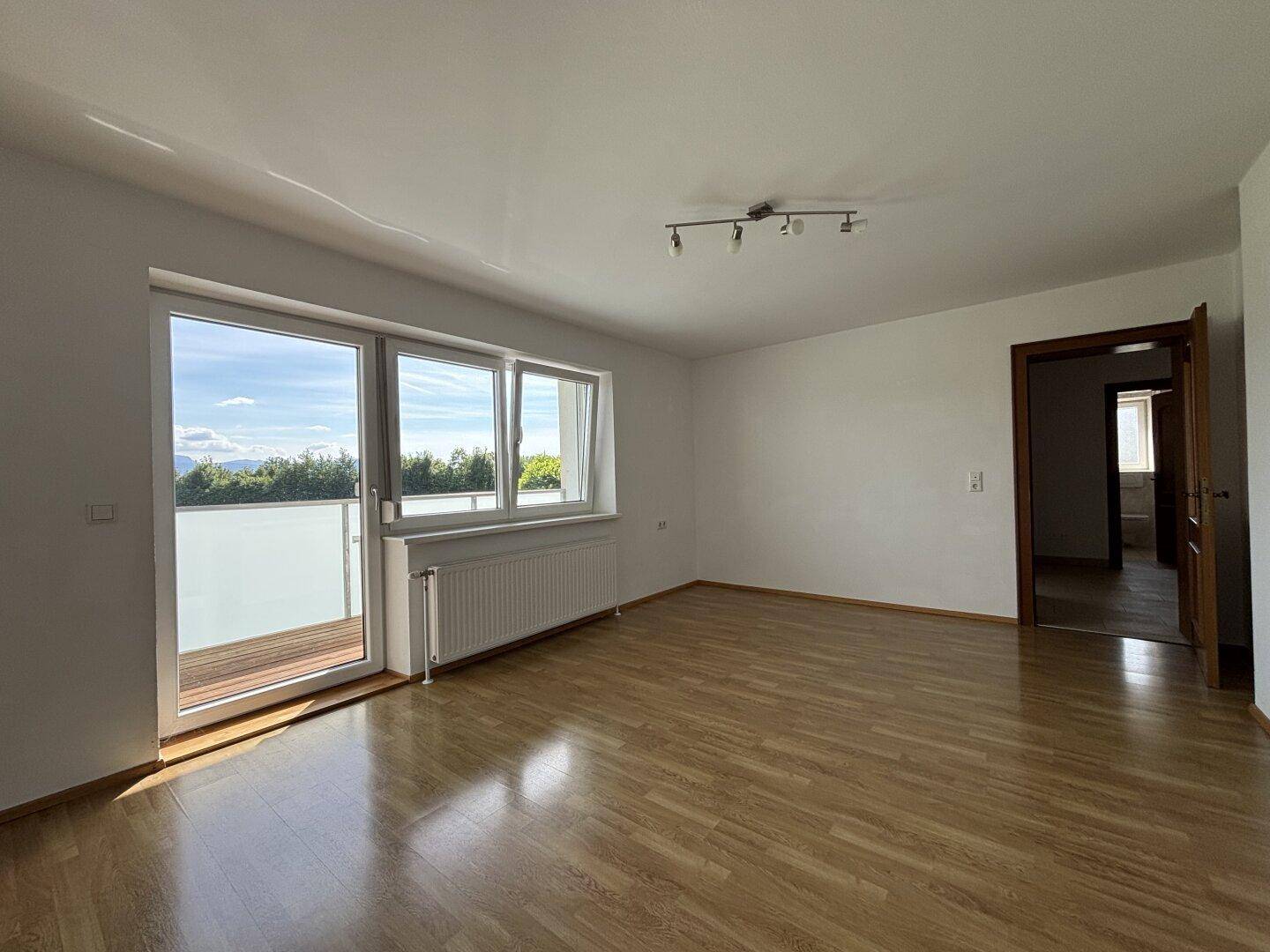 Helles Wohnzimmer mit Parkettboden, großem Fenster und Zugang zu einem Balkon mit Bergblick.