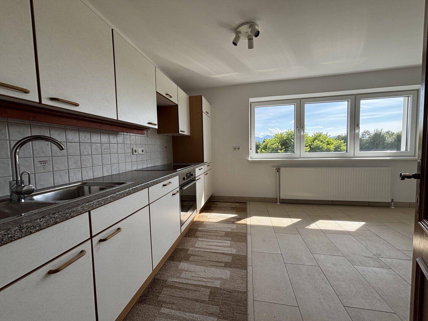Funktionale Küche mit weißen Schränken, Granit-Arbeitsplatte und Fliesenboden, hell durch großes Fenster.