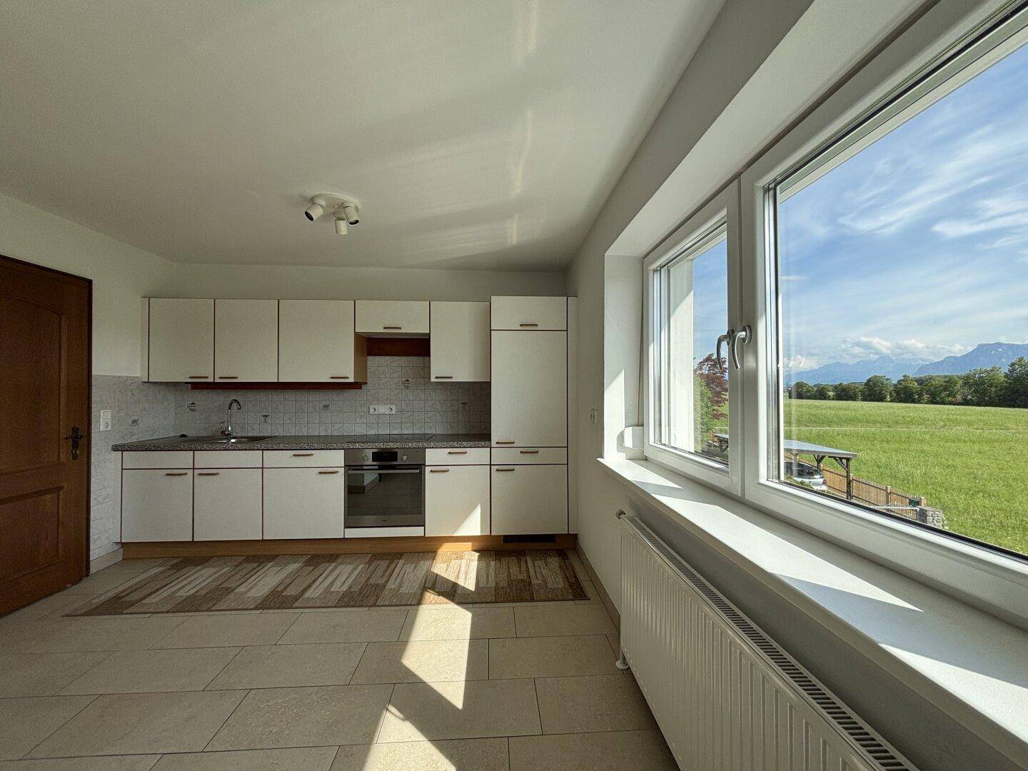 Geräumige Küche mit Einbauschränken und großem Fenster, das einen weiten Blick ins Grüne bietet.