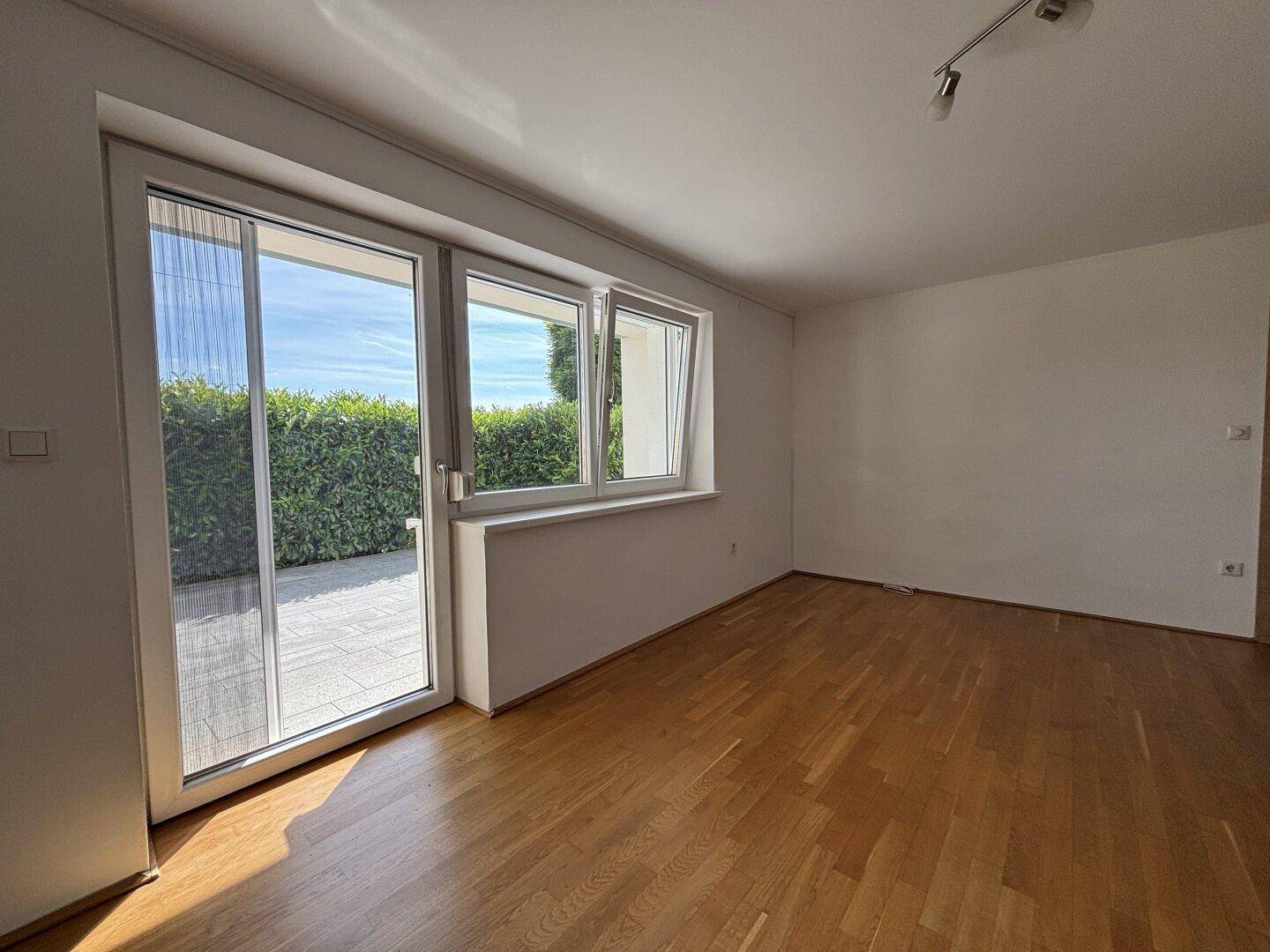 Heller Wohnraum mit Parkettboden und direktem Zugang zu einer Terrasse mit Blick auf die Hecke.