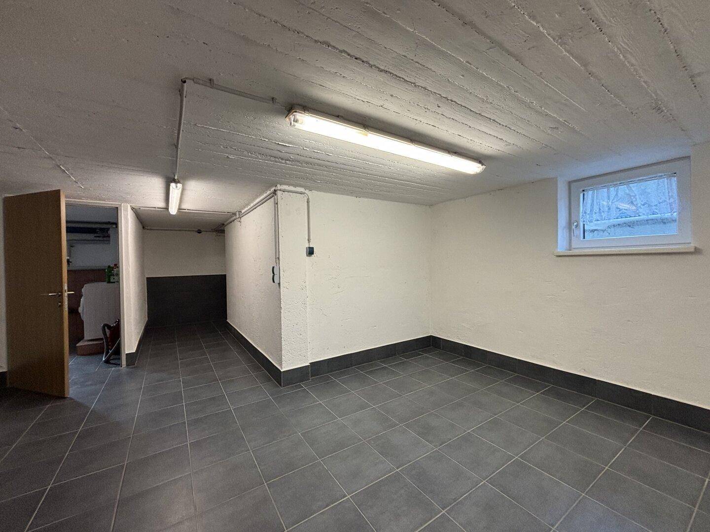 Sauberer Kellerraum mit Fliesenboden und kleinem Fenster, bietet zusätzlichen Stauraum.
