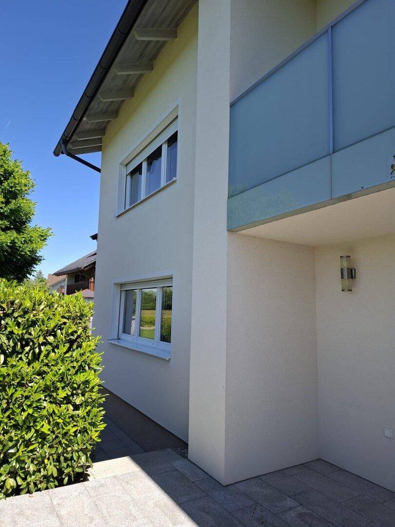 Seitenansicht des Hauses mit Balkon und einer gepflegten Hecke, die das Grundstück begrenzt.