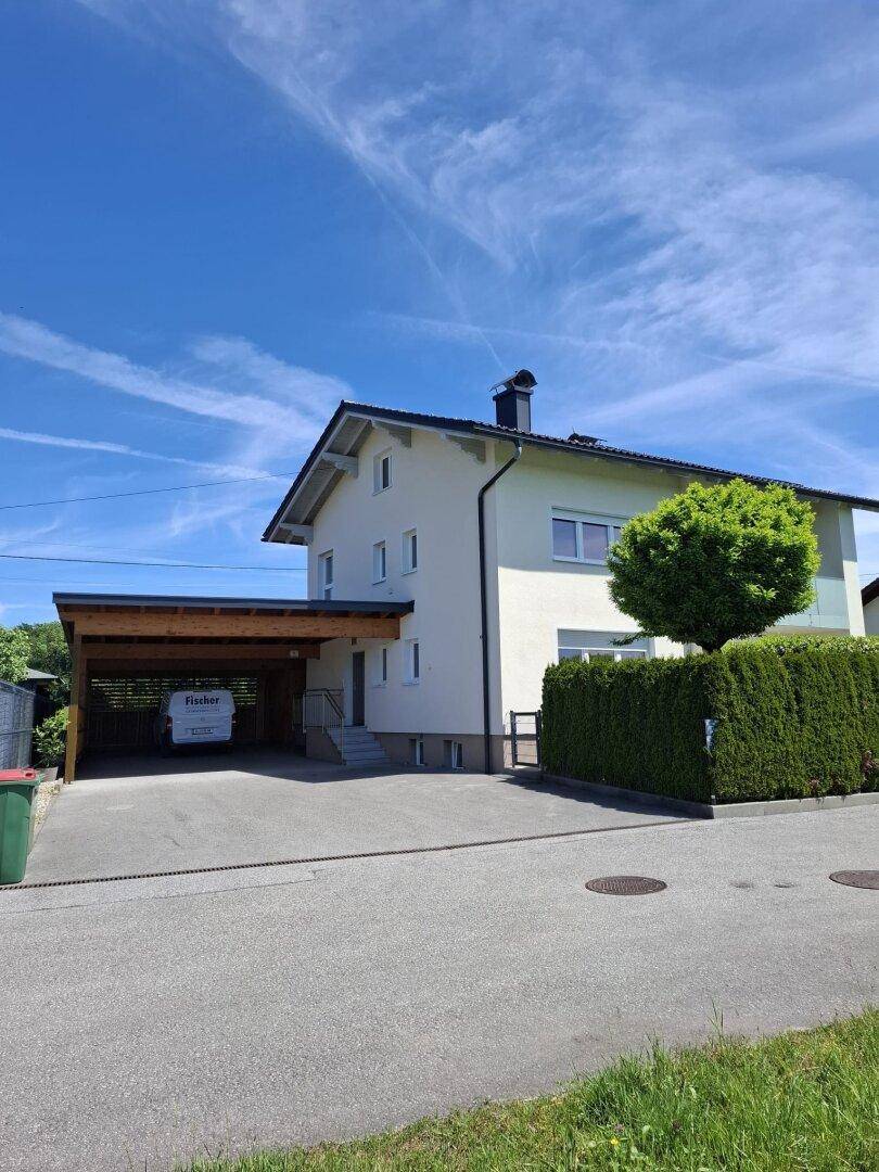 Ansicht des Einfamilienhauses mit Carport, Zufahrt und einer dichten Hecke entlang der Grundstücksgrenze.