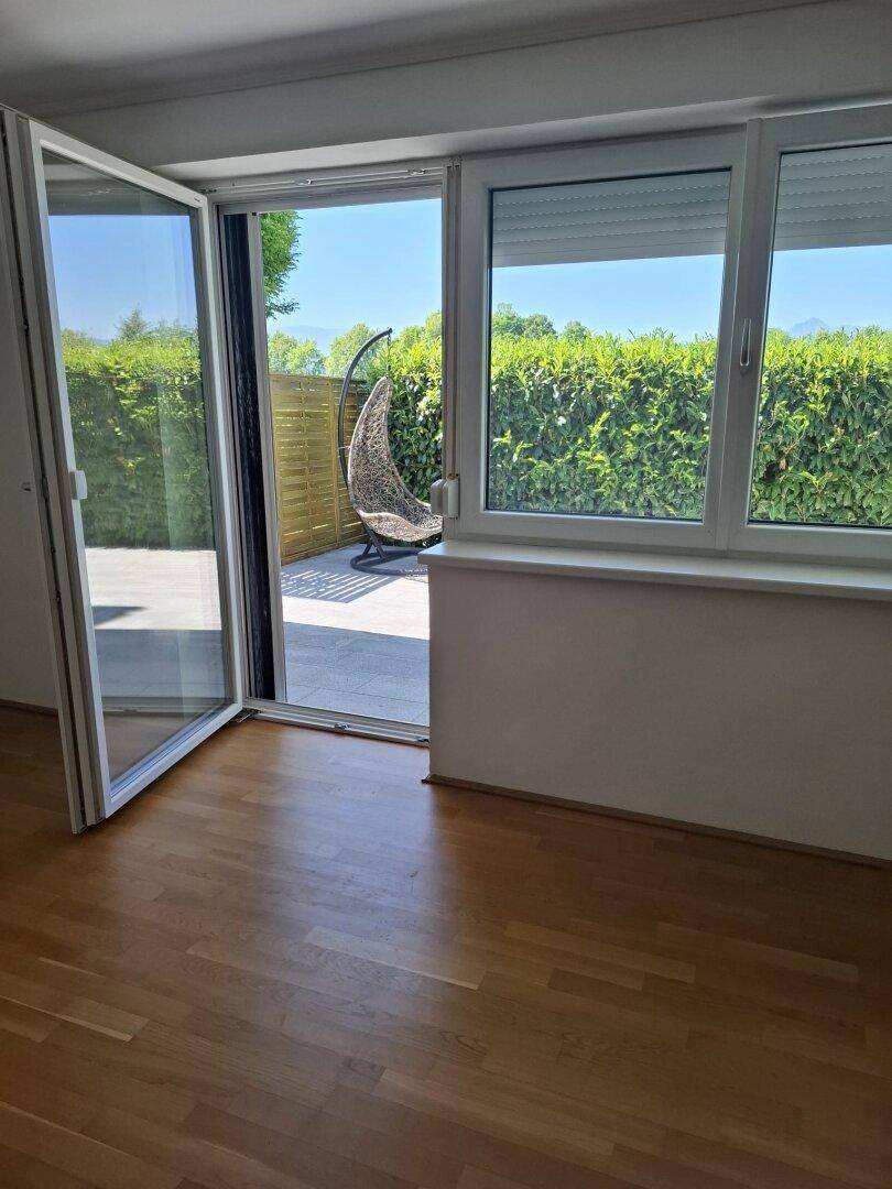 Heller Raum mit Parkettboden und direktem Zugang zu einer sonnigen Terrasse mit Hängesessel.